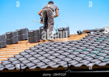 laborer with a chainsaw on the roof of a family house, building a roof from fired ceramic tiles Stock Photo