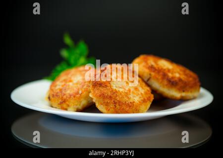 Cooked fried fish cutlets in a plate with herbs, isolated on a black background. Stock Photo