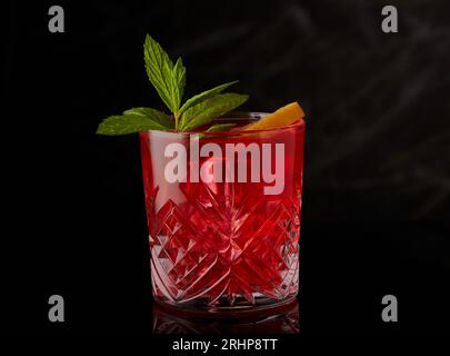 Red cocktail with ice and garnished with mint and a slice of lemon on a black background. Stock Photo