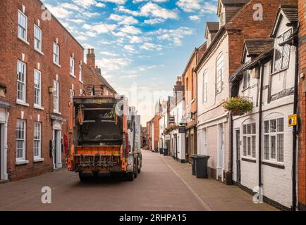 A municipal refuse collection vehicle collects rubbish or trash from wheelie bins at sunrise in Dam Street, Lichfield, Staffordshire, UK. Stock Photo