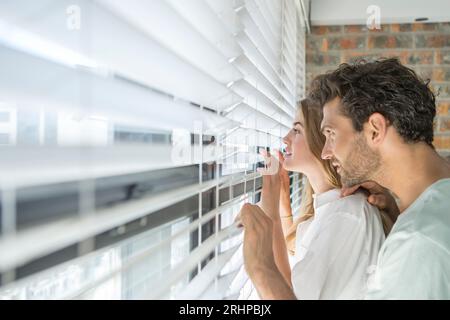 Couple looking through blind Stock Photo