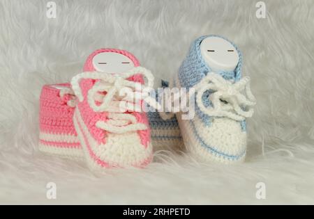 Knitted pink and blue booties on white fluffy blanket. Gender party concept idea. Booties for baby girl or boy for first step. Stock Photo
