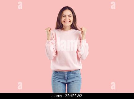 Woman in upbeat mood feels euphoric, celebrates success by raising hands with clenched fists. Stock Photo
