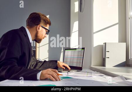 Man works with cadastral maps and city plans and uses spreadsheets on laptop computer Stock Photo