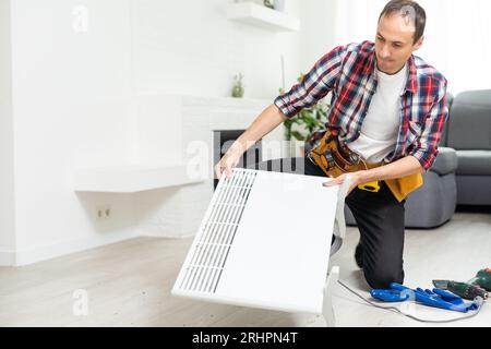 Workman mounting water heating radiator near the window in the white renovated living room, Image with copy space Stock Photo