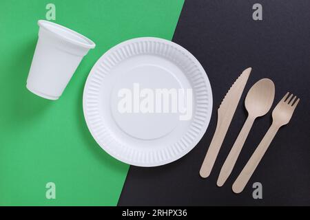 Paper plate, glass, wooden spoon, fork and knife on two-tone background, top view Stock Photo