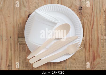 Paper plate, glass, wooden spoon, fork and knife on old wood, top view. Disposable tableware Stock Photo