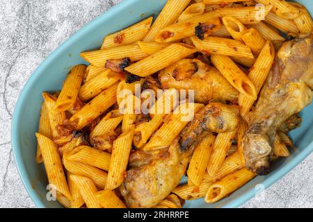 Penne pasta and chicken drumsticks cooked in a tomato and herb sauce in a ceramic dish. On a concrete background Stock Photo