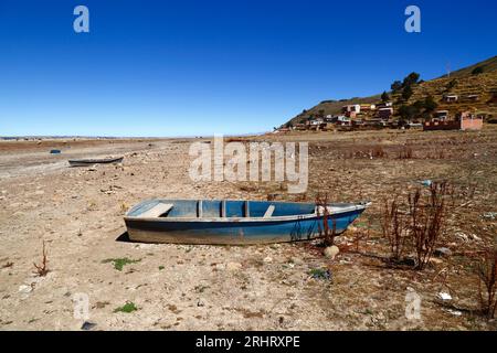 Lake Titicaca, BOLIVIA; August 18th 2023: Wooden rowing boats on the dried up shore of Cohana Bay on the Inner Lake / Huiñay Marka (the smaller part of Lake Titicaca) near the village of Cohana (in the background). Water levels in Lake Titicaca are approaching the record low level set in 1996, the lowest since Bolivia's weather service (Senhami) started keeping records in 1974. Many are blaming climate change; the last few years have been drier than normal and El Niño is currently strengthening in the Pacific Ocean off South America. Stock Photo