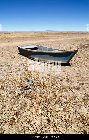 Lake Titicaca, BOLIVIA; August 18th 2023: A wooden rowing boat and dead totora reeds on the dried up shore of Cohana Bay on the Inner Lake / Huiñay Marka (the smaller part of Lake Titicaca) near the village of Cohana. Water levels in Lake Titicaca are approaching the record low level set in 1996, the lowest since Bolivia's weather service (Senhami) started keeping records in 1974. Many are blaming climate change; the last few years have been drier than normal and El Niño is currently strengthening in the Pacific Ocean off South America. Stock Photo