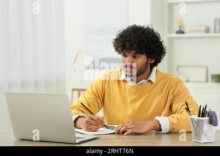 Handsome man taking notes near laptop in room Stock Photo