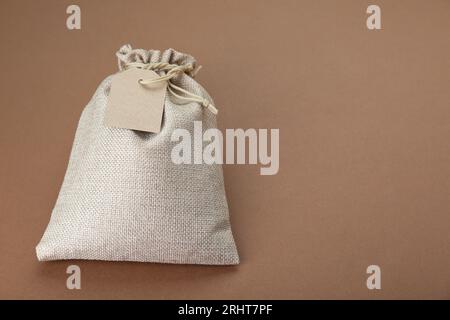 Tied burlap bag with tag on brown background. Space for text Stock Photo