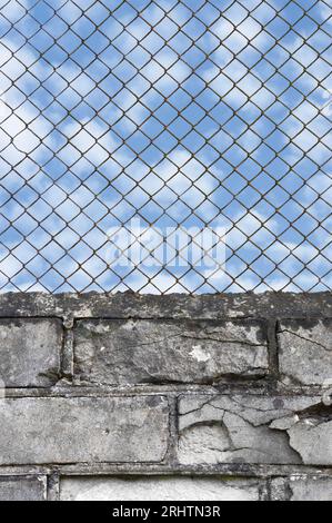 Rusty chain link fence, white grey brick wall texture background, blue summer sky clouds, vertical isolated old aged weathered rusted natural pattern Stock Photo