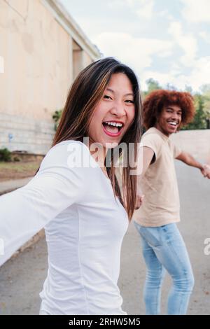 Vertical point view portrait of a multiracial group of friends walking holding hands. pov of young people having fun running hand in hand. First person perspective of three happy teenagers enjoying. High quality photo Stock Photo