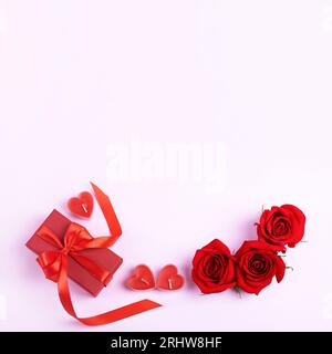 Red roses and red gift box with a red satin ribbon bow and candles in the shape of hearts. Romantic background with space for text. Happy greeting car Stock Photo