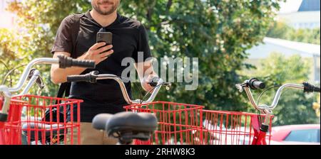 Bicycle sharing system, young urban man smiling and using his mobile phone for renting the bicycle. Stock Photo