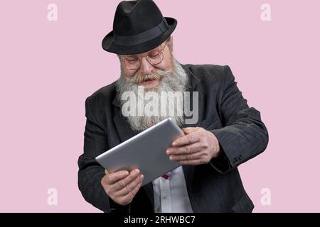 Portrait of excited aged man with tablet pc. Isolated on pink. Stock Photo