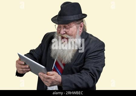 Portrait of excited senior man with tablet pc. Isolated on yellow. Stock Photo