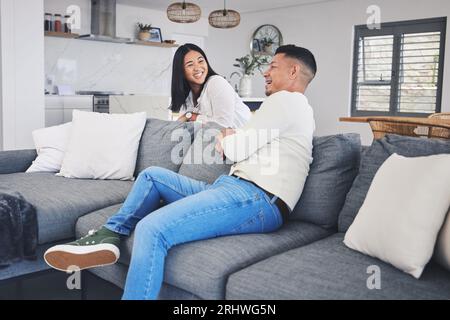 Happy, love and couple relax on a sofa bond, talking and enjoying weekend in their home together. Smile, conversation and woman with man in living Stock Photo