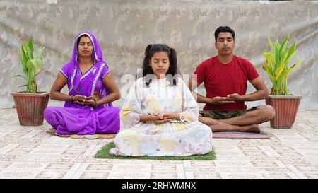 Meditation, practicing breathing yoga exercises. Wellness hobby concept,  Happy fit family of young parents and little kids sitting together on floor Stock Photo