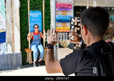Quirky little spot with swing and “Serendipity Concept” street art which attracts tourists, man photographing woman with phone Stock Photo