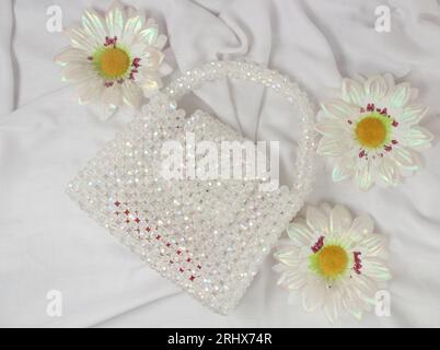 Handmade white purse made with bright beads on gray fabric with fake daisies flower. Top view. Stock Photo