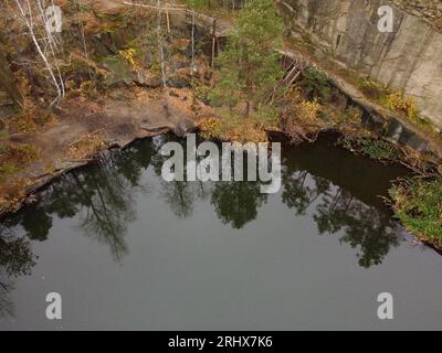 Picturesque aerial view of landscape with emerald lake and rocks in the middle of a coniferous autumn forest in Korostyshiv granite quarry, Zhytomyr d Stock Photo
