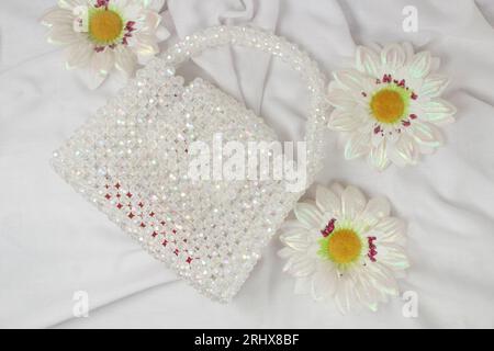 Handmade white purse made with bright beads on gray fabric with fake daisies flower. Top view. Stock Photo