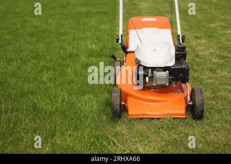 Top view of modern orange-grey electric lawn mower cutting bright lush green grass. Gardening work tools. Rotary lawn mower machine on lawn. Professio Stock Photo