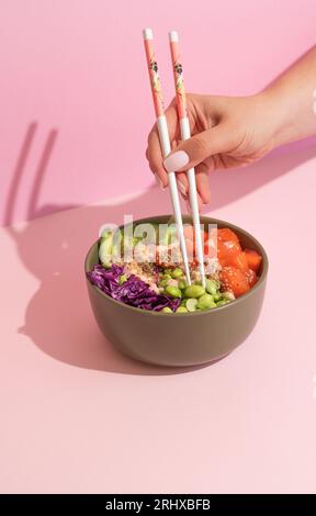 Hands eating poke bowl with salmon on pink background Stock Photo