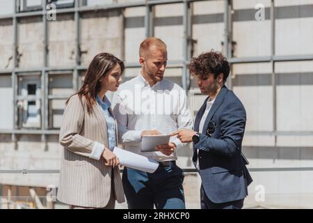 Young architect pointing at blueprint on the tablet. Construction engineers discussing blueprint on tablet while working in a construction area in the Stock Photo