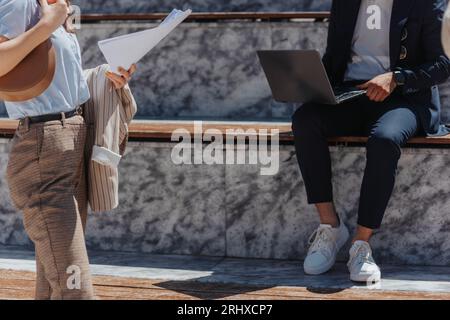 Business people working outdoors. Businessman working on lap top remotely. Businesswoman working on tablet out in the city. Cropped photo Stock Photo