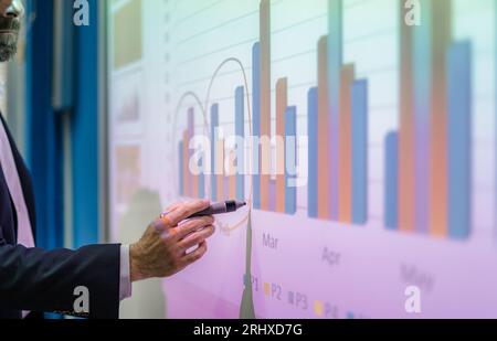 University professor giving lecture to students, writing on smart board, explaining charts Stock Photo