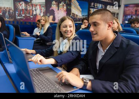 Young and well-dressed students smiling and working together on their laptops in class Stock Photo