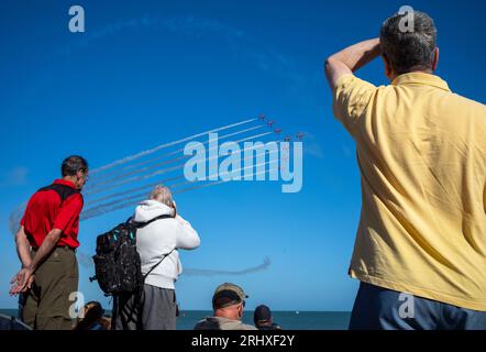 Eastbourne, UK. 19 Aug 2023. People on Eastbourne beach watch as the world famous RAF display team The Red Arrows fly past the seafront at the annual Eastbourne Airbourne, an international airshow. The show runs for four days with flying displays along the seafront. Stock Photo