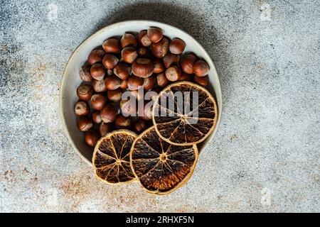 Top view of fresh chestnuts placed in ceramic bowl with dried orange slices in a concrete background Stock Photo