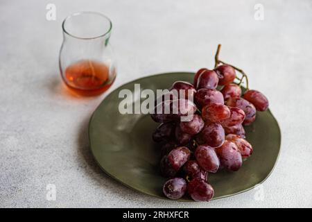 High angle of red Champagne grape variety served on dark plate near pink champagne wine in glass against gray background Stock Photo
