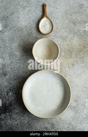 Top view of ceramic tableware set consisting of bowl, plate and wooden spoon placed on gray surface Stock Photo