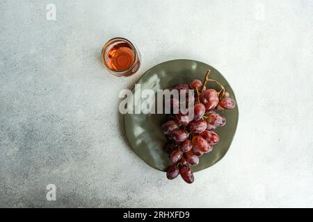 Top view of red Champagne grape variety served on dark plate near pink champagne wine in glass against gray background Stock Photo