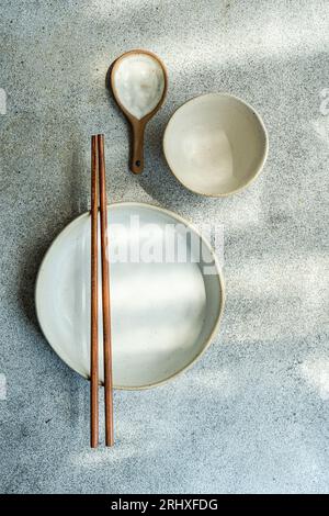 Top view of ceramic tableware set consisting of bowl, plate, wooden spoon and chopsticks placed on gray surface Stock Photo