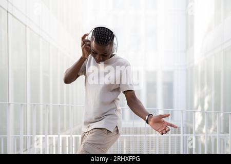 Side view of positive African American teenage male in casual clothes and headphones dancing while listening to music in wireless headphones on bright Stock Photo