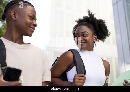 Portrait of positive young African American teenage couple in casual clothes with Afro hairstyle and backpacks smiling and looking at each other Stock Photo