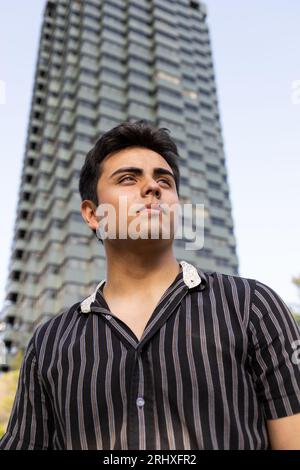 Low angle view of Caucasian handsome young man wearing black shirt looking away thoughtfully while standing against modern building in city Stock Photo