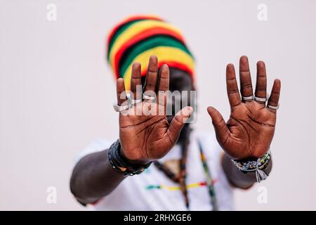 Blurred African American man in colorful hat standing and looking at camera while putting hands in front of the camera against white background Stock Photo