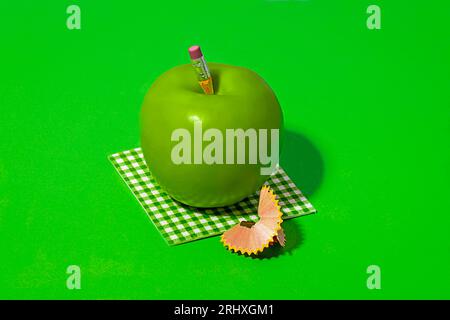 Pencil on healthy Granny Smith apple placed on check pattern cloth near pencil shavings on bright green background Stock Photo