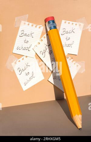 Yellow colored pencil with red eraser and with broken tip placed leaning on beige wall with shadow near pasted papers from spiral notebook with messag Stock Photo