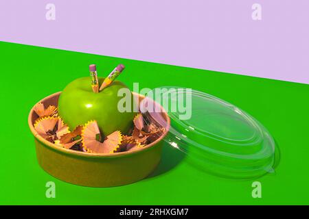 From above of healthy apple surrounded with pencil shavings in lunch box placed on green and white background representing concept of zero waste Stock Photo