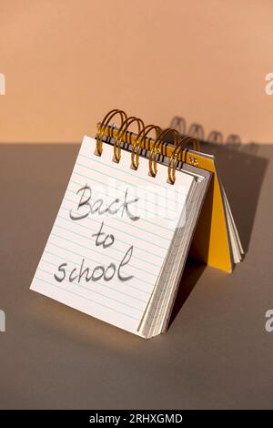 From above of opened spiral notebook with hardcovers and parallel lines page with message back to school written with pencil and with shadow placed on Stock Photo