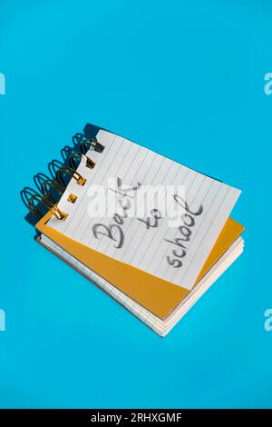 From above of opened spiral notebook with hardcovers and parallel lines page with message back to school written placed against blue wall Stock Photo