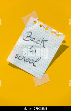Spiral bound notebook page parallel lines holes on top and with pencil message back to school pasted with transparent sticker on yellow colored wall i Stock Photo